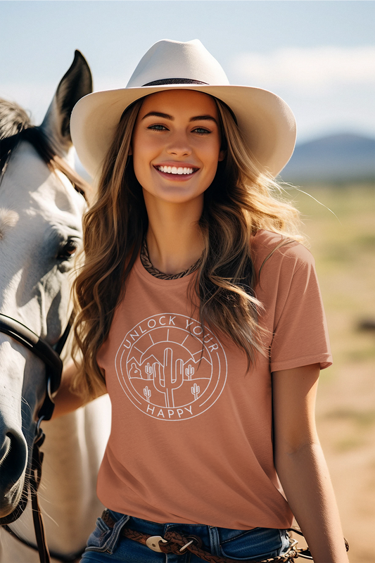 A t-shirt featuring a desert scene graphic with cacti, desert mountains, and a bright sun. The text 'Unlock Your Happy' is integrated into the design, capturing a serene vibe.